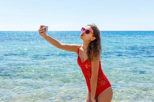 Verano chica de vacaciones de playa tomando foto autofoto móvil divertido con teléfono inteligente. Chica usando gafas de sol rojas posando para selfie —  Fotos de Stock