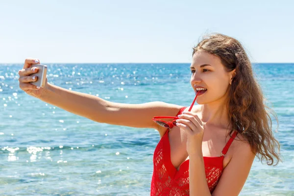 Сексуальная девушка на пляже с удивленным выражением лица смотрит на телефон и делает селфи — стоковое фото