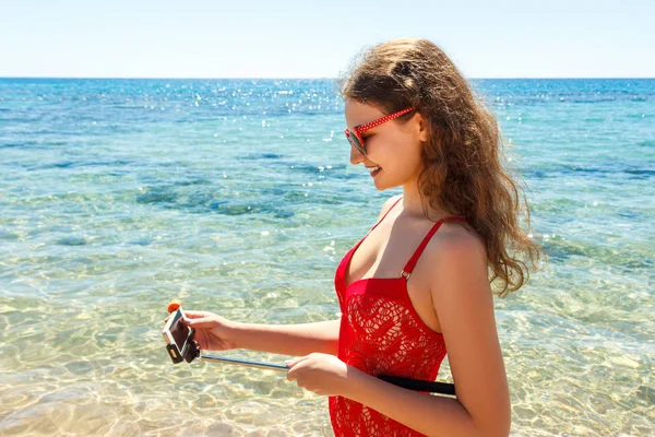 Chica en la playa con un teléfono celular haciendo selfie en el día soleado —  Fotos de Stock
