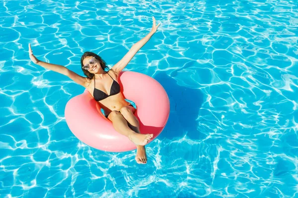 Bikinili genç mutlu kız pembe bir daire sahip havuzunda yüzüyor