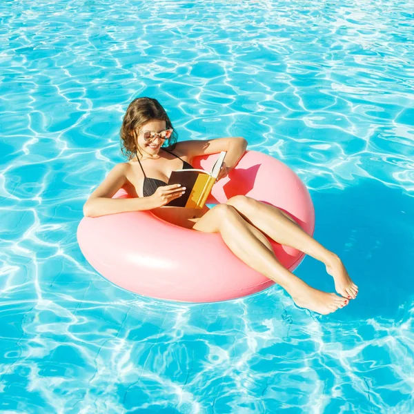 Bikini chica con gafas de sol relajado y libro de lectura en rosa anillo de piscina inflable —  Fotos de Stock