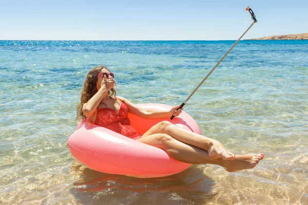 Красивая молодая женщина расслабляется и делает селфи на надувной пончик в море — стоковое фото
