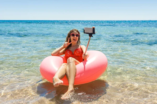 Menina sorrindo feliz faz a selfie que flutua no donut inflável no mar. tempo de férias — Fotografia de Stock