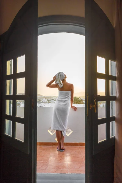 Eine Frau in einem weißen Handtuch steht auf einer Terrasse mit Blick auf die Berge in einem Hotelzimmer — Stockfoto