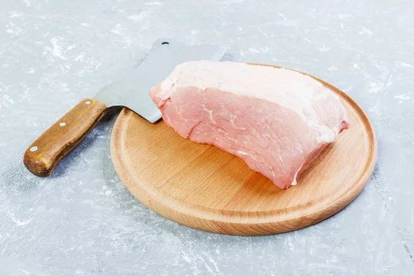Grande pedaço fresco de porco em uma tábua de corte de madeira redonda com machado de cozinha. Visão superior sobre fundo de concreto cinza — Fotografia de Stock