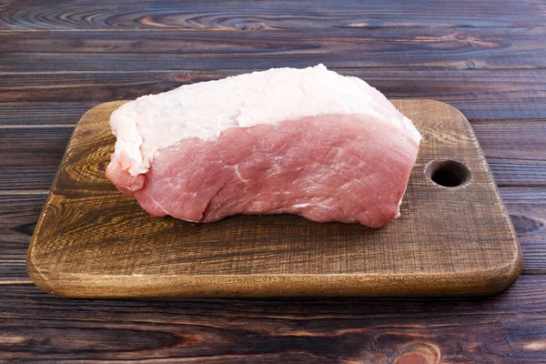 Segar sepotong besar daging babi di papan potong kayu bulat. Tampilan atas pada latar belakang kayu — Stok Foto