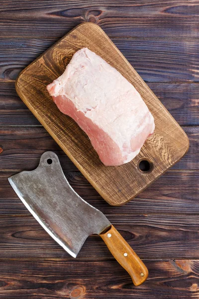 Raw cut of pork shoulder on board with knife or Kitchen ax. cleaver with fresh raw meat on black wooden background