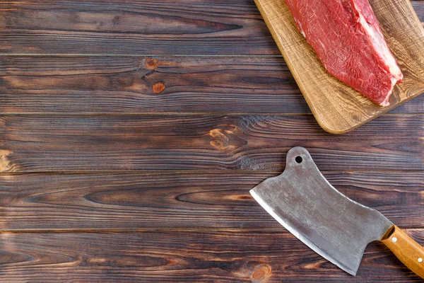 Friss sertéshús egy kerek fa vágódeszka a konyha ax nagy darab. Felülnézet szürke beton alapon — Stock Fotó