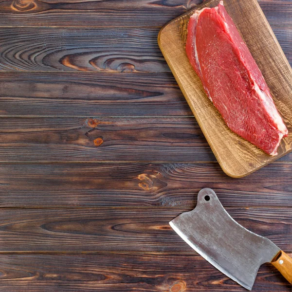 Vintage cleaver and raw beef steak on dark wooden background. copy space Royalty Free Stock Images