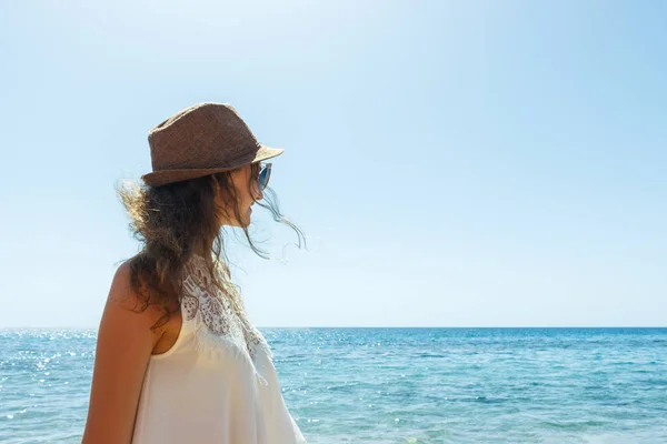 Ung kvinna i hatt står på en strand och tittar till en havshorisonten — Stockfoto