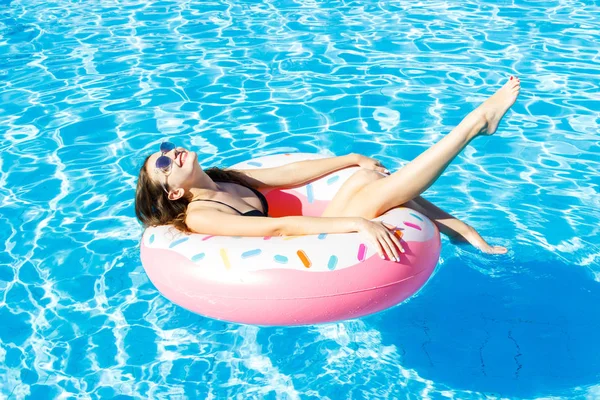 Hermosa joven con círculo rosa relajante en la piscina azul —  Fotos de Stock