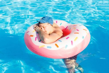top view of young drunk guy swim with pink circle in pool. drunk guy on vacation in the hotel clipart