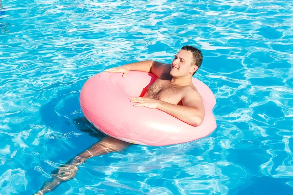 Young man is floating on inflatable air ring circle in pool with blue water