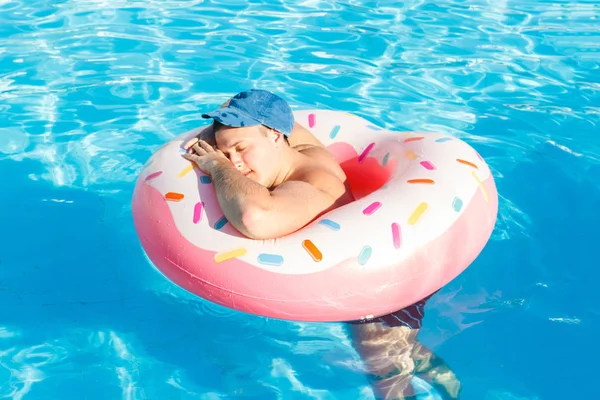 top view of young drunk guy swim with pink circle in pool. drunk guy on vacation in the hotel