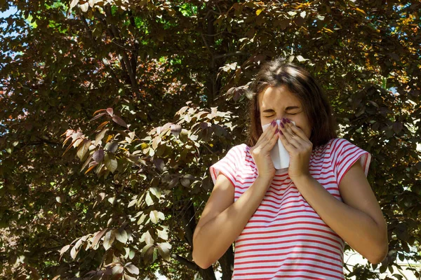 Ung flicka med allergi i höst park. Nysa flicka blåser näsan i en servett — Stockfoto