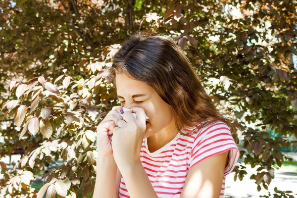 若い可愛い女の子がツリーの前に鼻をかみます。春のアレルギーの概念 — ストック写真