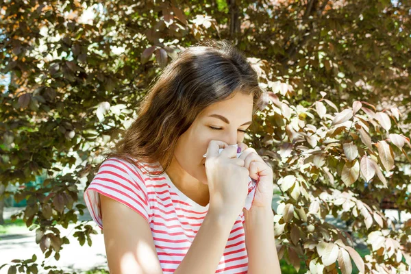 Konsep Alergi. Bersin gadis muda dengan wiper hidung antara pohon mekar di taman — Stok Foto