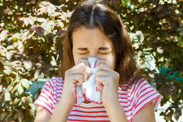 公園で咲く木の中でナプキンでくしゃみをする少女。アレルギーの概念 — ストック写真