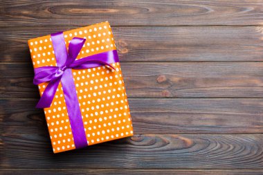 Koyu ahşap masanın üzerinde renkli bir fiyonk olan güzel bir hediye kutusu. Tasarımınız için fotokopi alanı olan en iyi görünüm pankartı