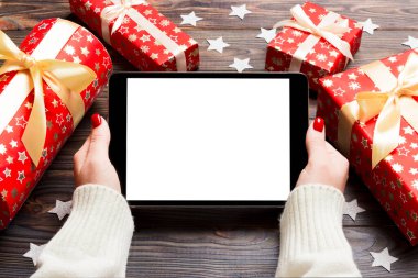 Hediye kutuları ve kar tanelerinden yapılmış ahşap Noel arka planında bir tablet tutan kadınların üst görüntüsü. Yeni yıl tatili konsepti. Model