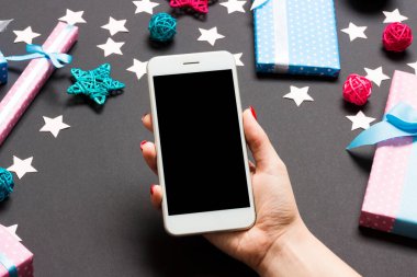 Bayramlık siyah arka planda kadın elinin telefonunun üst görüntüsü. Noel süsleri. Yeni yıl tatili. Model