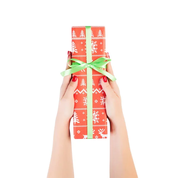 Dámské ruce dát zabalené vánoční nebo jiné sváteční ručně vyrobené dárek v červeném papíru se zelenou stuhou. Izolované na bílém pozadí, horní pohled. koncept díkůvzdání dárkové krabice — Stock fotografie
