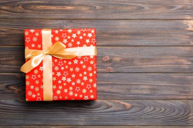 Koyu ahşap masanın üzerinde renkli bir fiyonk olan güzel bir hediye kutusu. Tasarımınız için fotokopi alanı olan üst görünüm. Noel konsepti