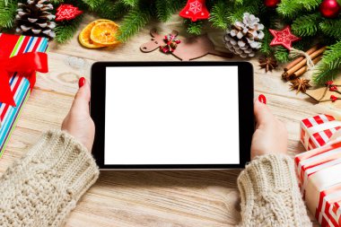 Kadın ellerinin, köknar ağacı ve şenlikli süslemelerden yapılmış ahşap Noel arka planında bir tablet taşıdığı en üst görüntü. Yeni yıl tatili konsepti. Model