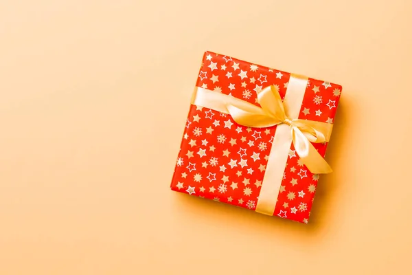 Zabalené vánoční nebo jiné sváteční ručně vyráběné dárek v papíru se zlatou stuhou na oranžovém pozadí. Dárek box, dekorace dárku na barevném stole, horní pohled s kopírovacím prostorem — Stock fotografie