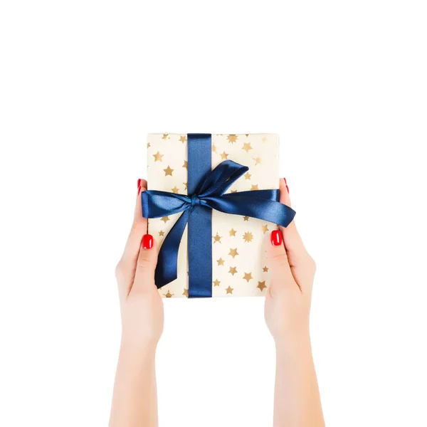 Vrouw handen geven verpakt Kerstmis of andere vakantie met de hand gemaakt in goud papier met blauw lint. Geïsoleerd op witte achtergrond, bovenaanzicht. dankzegging Geschenkdoos concept — Stockfoto