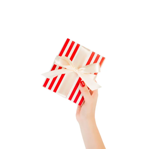 Dámské ruce dát zabalené vánoční nebo jiné sváteční ručně vyrobené dárek v červeném papíru se zlatou stuhou. Izolované na bílém pozadí, horní pohled. koncept díkůvzdání dárkové krabice — Stock fotografie