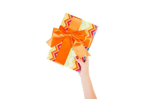 Vrouw handen geven verpakt Kerstmis of andere vakantie met de hand gemaakt in gekleurd papier met oranje lint. Geïsoleerd op witte achtergrond, bovenaanzicht. dankzegging Geschenkdoos concept — Stockfoto