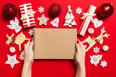 Kadın elinin rengarenk arka planda notlar aldığına dair üst görünüm. Yeni yıl süslemeleri ve oyuncakları. Noel zamanı konsepti