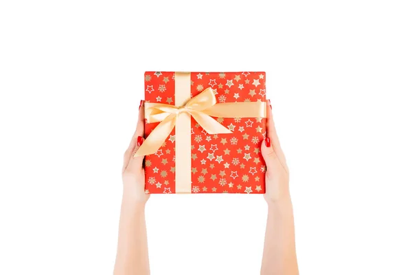 Kobiece dłonie dają zawinięte Boże Narodzenie lub inny świąteczny prezent ręcznie w czerwony papier ze złotą wstążką. Izolacja na białym tle, widok z góry. dziękczynienie koncepcja pudełko prezent — Zdjęcie stockowe
