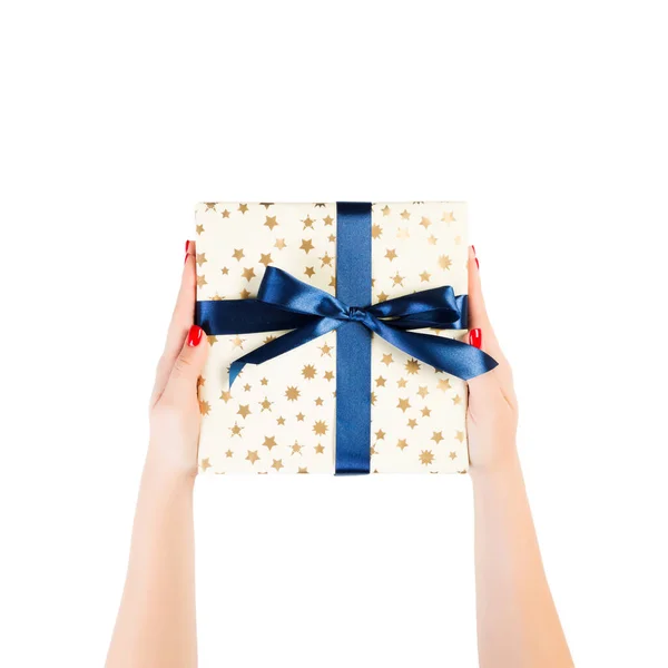 Dámské ruce dát zabalené Vánoce nebo jiné sváteční ručně vyrobené dárek ve zlatém papíru s modrou stuhou. Izolované na bílém pozadí, horní pohled. koncept díkůvzdání dárkové krabice — Stock fotografie