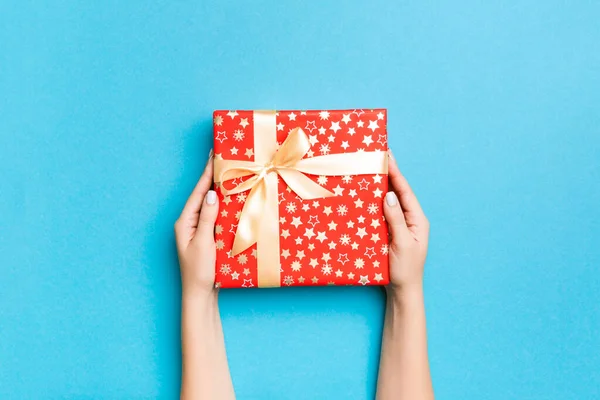 Brazos de mujer sosteniendo caja de regalo con cinta de color en ba mesa azul —  Fotos de Stock