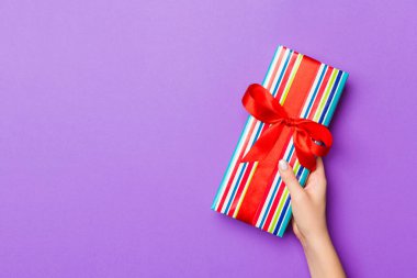 Kadınların düz uzanmış elleri hediye paketi ve dekore edilmiş mor arka planda fotokopi alanı ile. Noel ve tatil konsepti