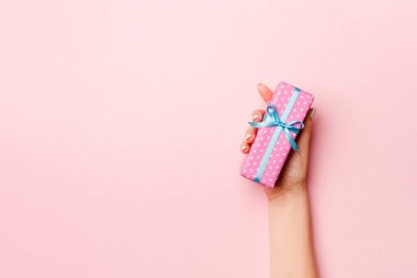 Kadının elleri çizgili hediye kutusunu tutuyor ve canlı mercan arka planında renkli kurdele var. Noel konsepti ya da diğer tatil el yapımı hediye kutusu, kopya alanı olan konsept üst görünüm