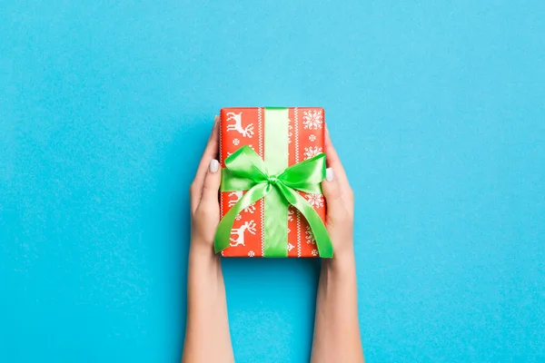 Woman arms holding gift box with colored ribbon on blue table background, top view and copy space for you design