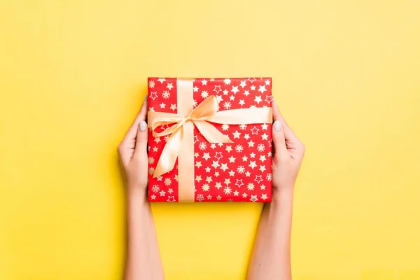 Brazos de mujer que sostienen la caja de regalo con cinta de color sobre fondo de mesa amarillo, vista superior y espacio de copia para su diseño —  Fotos de Stock