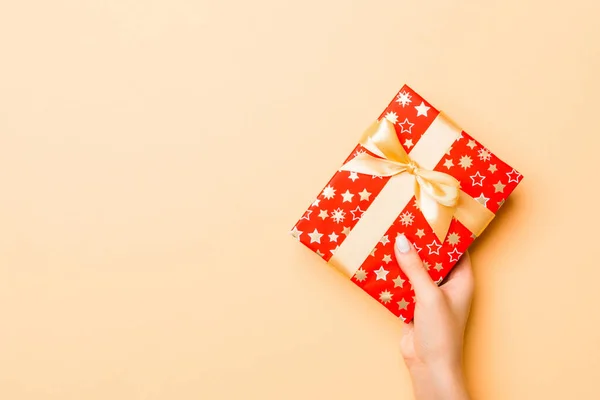 Colocación plana de manos de mujer sosteniendo regalo envuelto y decorado con arco sobre fondo dorado con espacio de copia. Concepto de Navidad y vacaciones —  Fotos de Stock