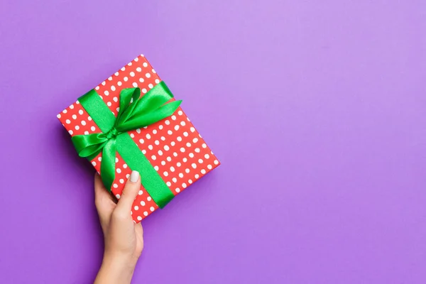 Pose plate de mains de femme tenant cadeau enveloppé et décoré avec arc sur fond violet avec espace de copie. Noel et concept de vacances — Photo