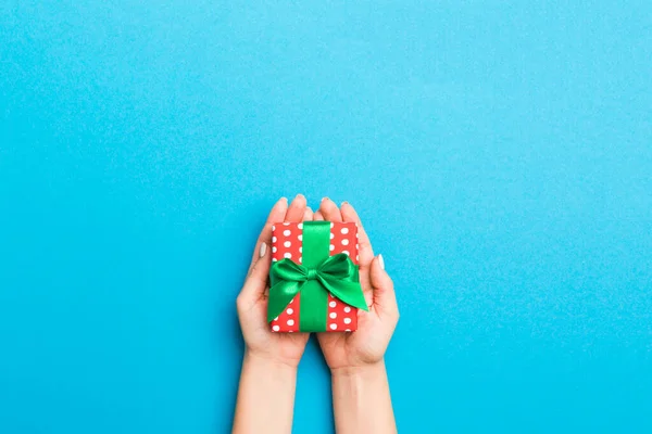 Woman arms holding gift box with colored ribbon on blue table background, top view and copy space for you design