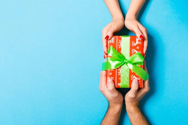 Widok dwóch osób dzielących się prezentem na kolorowym tle. Koncepcja świąt i niespodzianek. Zamknij się. — Zdjęcie stockowe