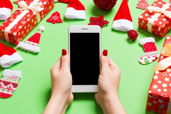 A telefon felső nézete női kézben ünnepi zöld háttérrel. Karácsonyi dekoráció. Szilveszterkor. Mockup — Stock Fotó