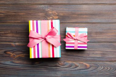 Koyu ahşap masanın üzerinde renkli bir fiyonk olan güzel bir hediye kutusu. Tasarımınız için fotokopi alanı olan en iyi görünüm pankartı