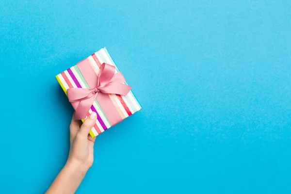 Woman arms holding gift box with colored ribbon on blue table ba