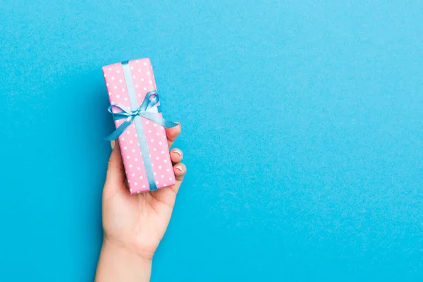 Woman arms holding gift box with colored ribbon on blue table ba