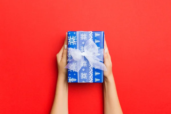 Vrouwelijke handen houden gestreepte geschenkdoos met gekleurd lint op r — Stockfoto