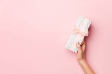 Kadının elleri çizgili hediye kutusunu tutuyor. Üzerinde renkli kurdele var.